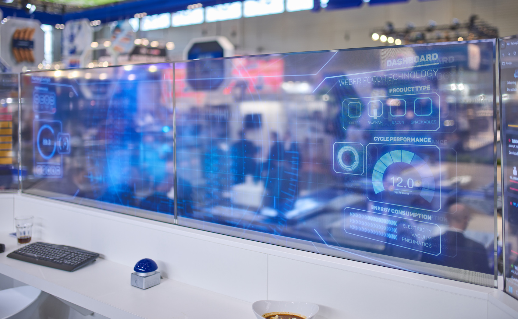 Seitliche Ansicht auf eine blaue hologrammartige Darstellung eines Interfaces auf einer Glasplatte, implementiert auf einem Messestand der Messe Anuga FoodTec.